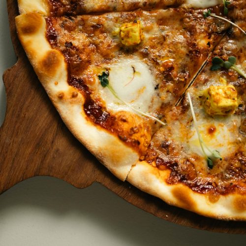 Delicious gourmet pizza featuring paneer and herb toppings on a wooden serving board.
